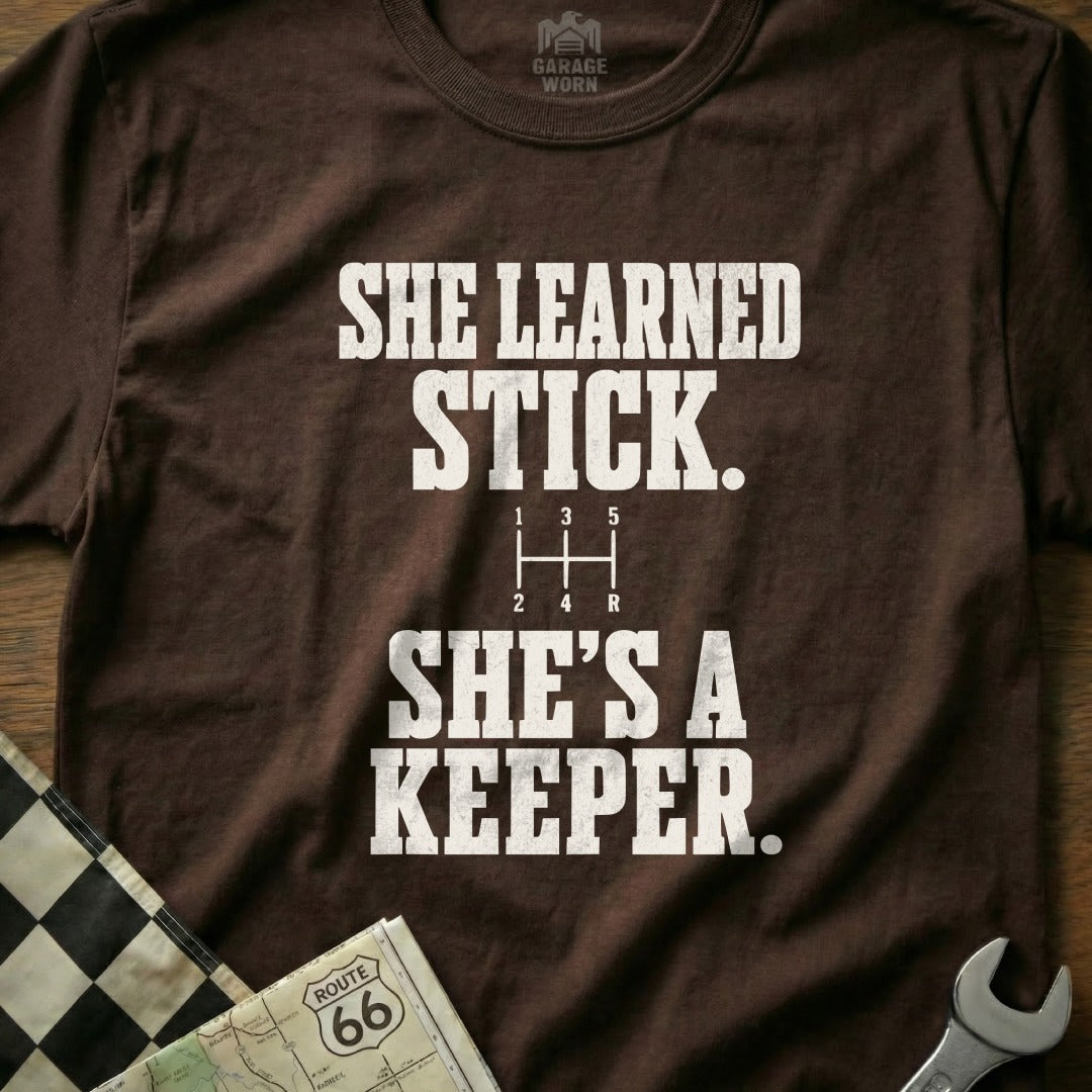 Brown t-shirt with "SHE LEARNED STICK. SHE'S A KEEPER." graphic.