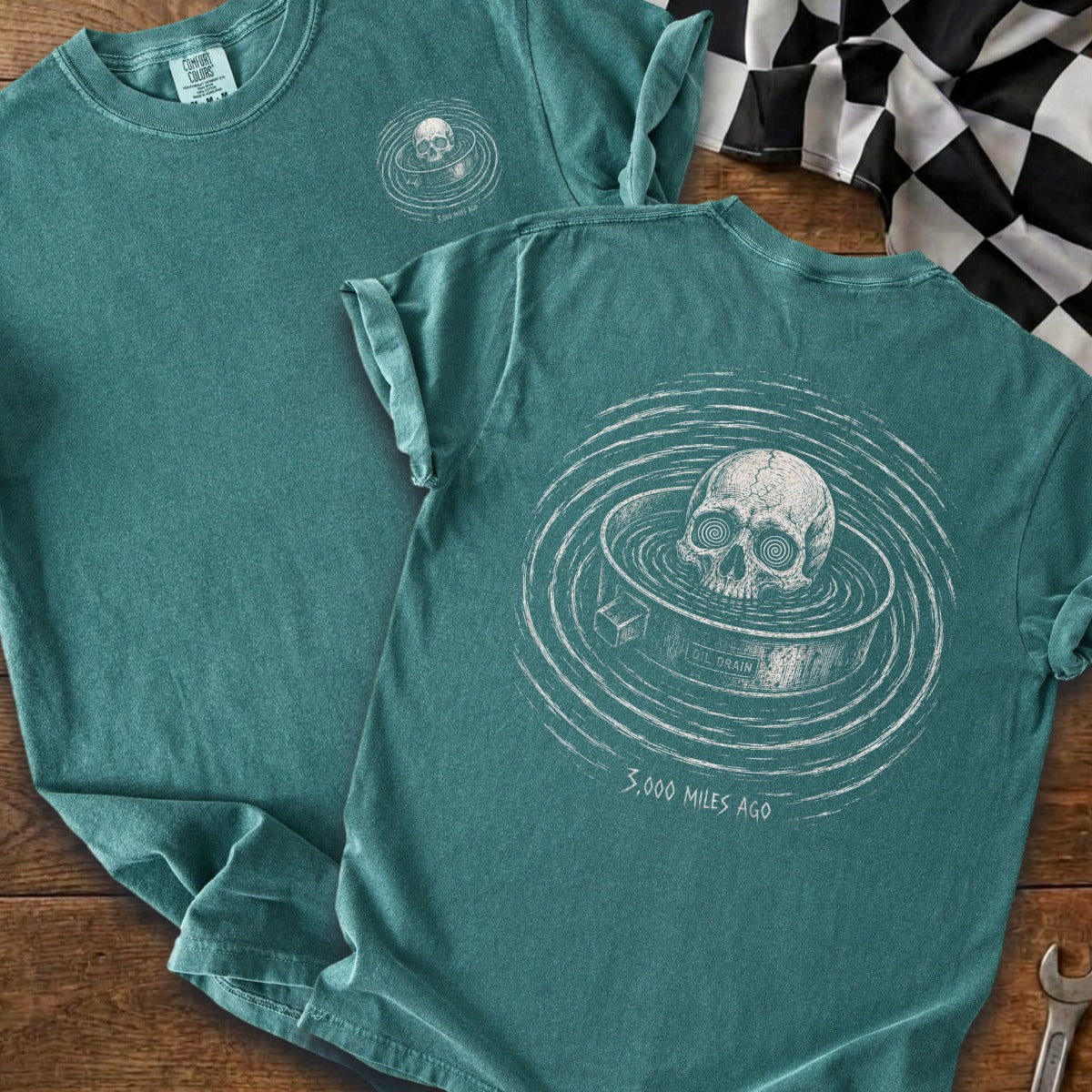 Teal t-shirt with skull in oil drain graphic and text "3,000 MILES AGO"