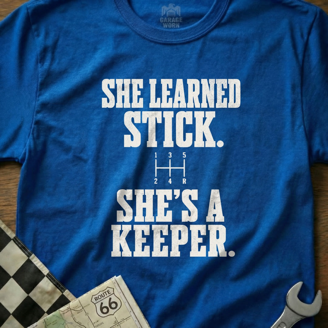 Blue t-shirt with "SHE LEARNED STICK. SHE'S A KEEPER." and gear shift graphic.