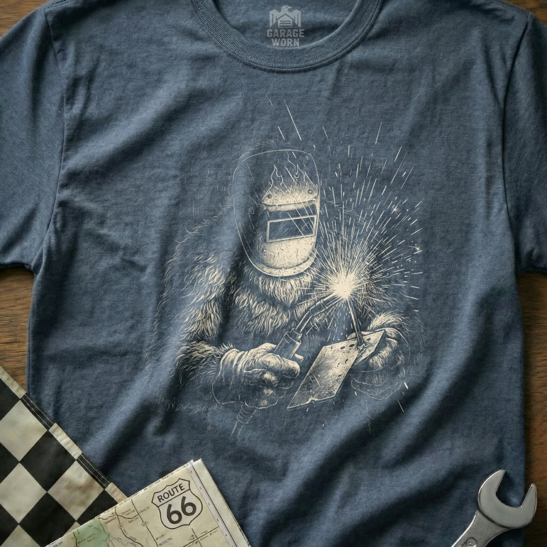 T-shirt featuring a Bigfoot welding with sparks flying, Route 66 map, and checkered flag.