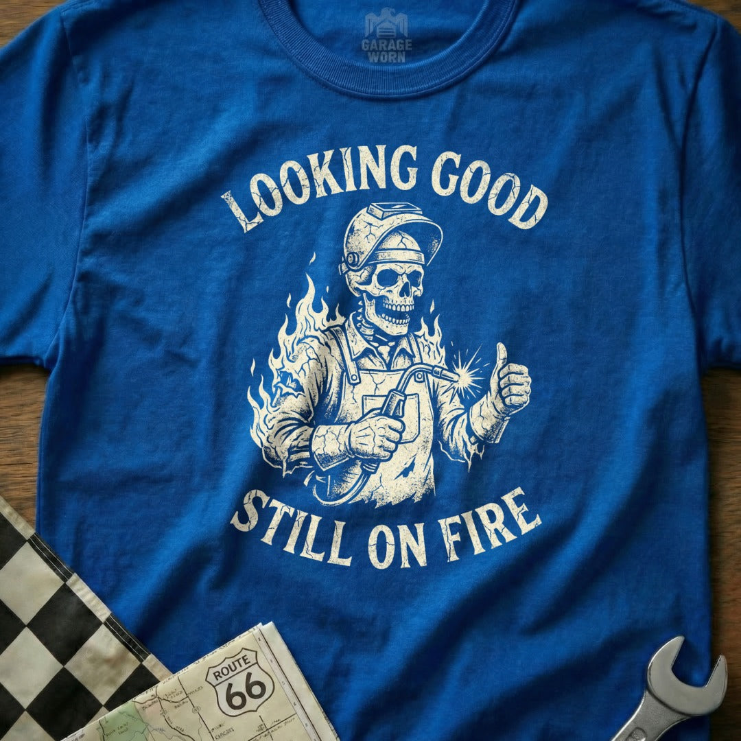 Blue t-shirt with a skeleton welder giving a thumbs-up and text "LOOKING GOOD STILL ON FIRE".