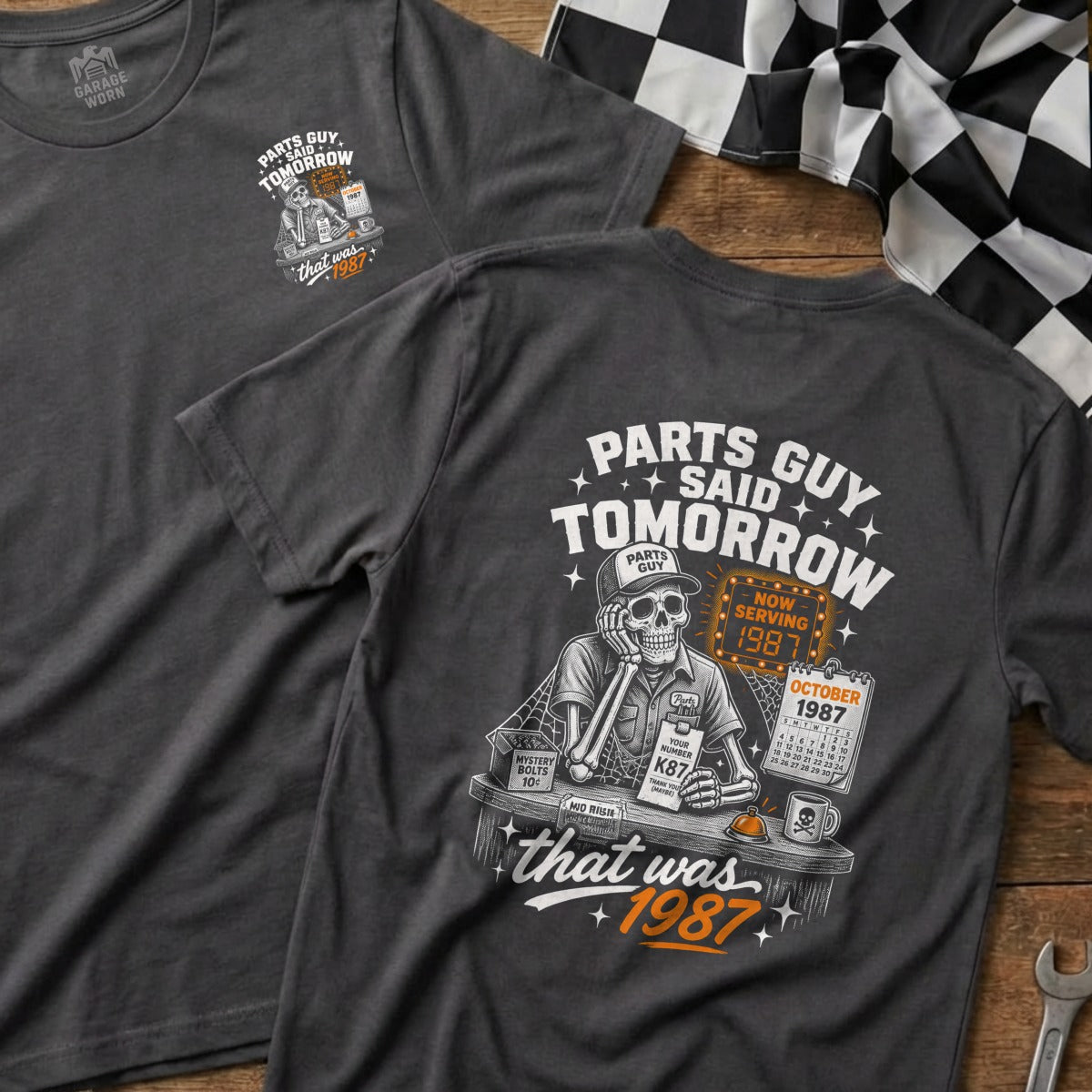 Dark gray t-shirt with a graphic of a skeleton, calendar, and text "Parts Guy Said Tomorrow That Was 1987".