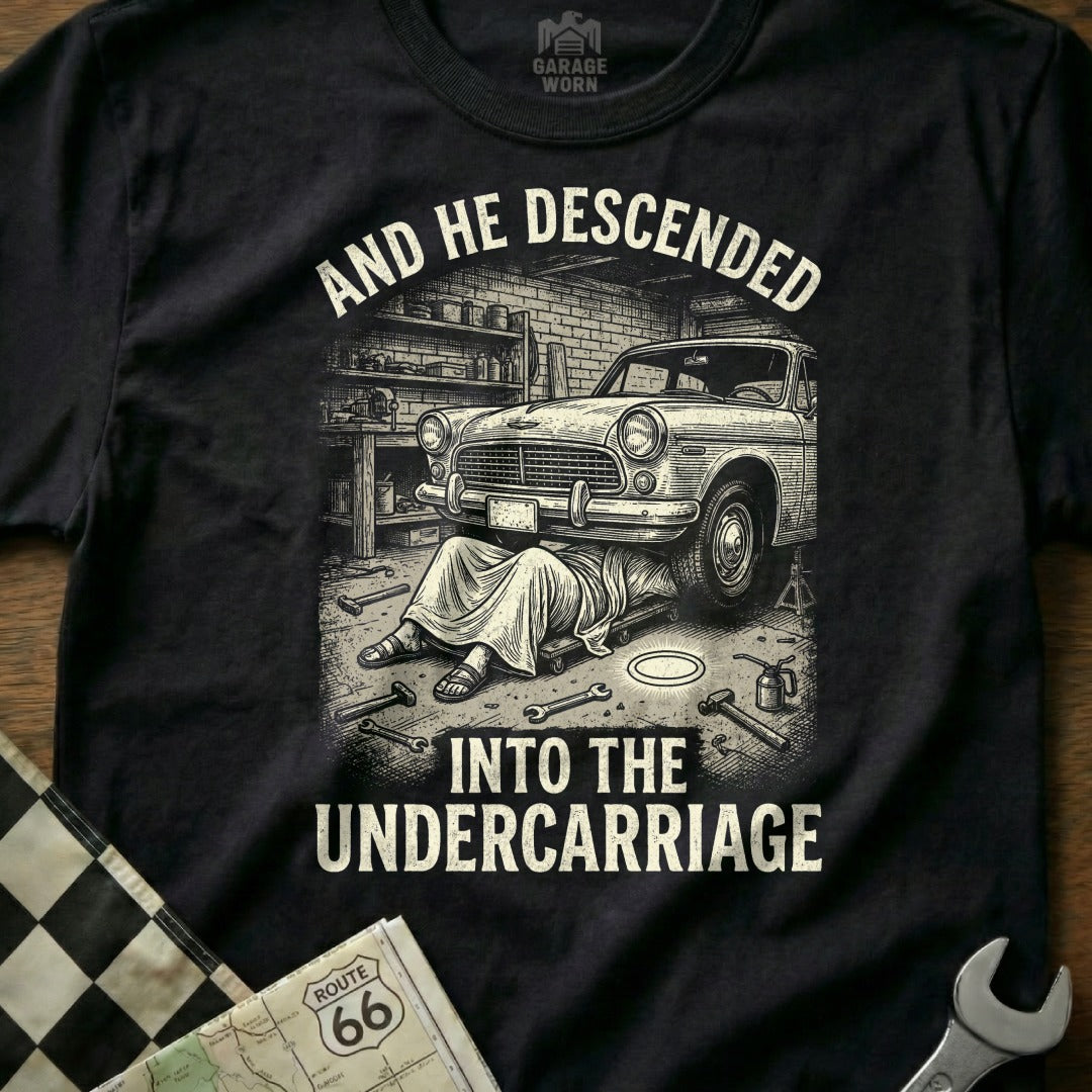T-shirt design with car being repaired under text "AND HE DESCENDED INTO THE UNDERCARRIAGE".