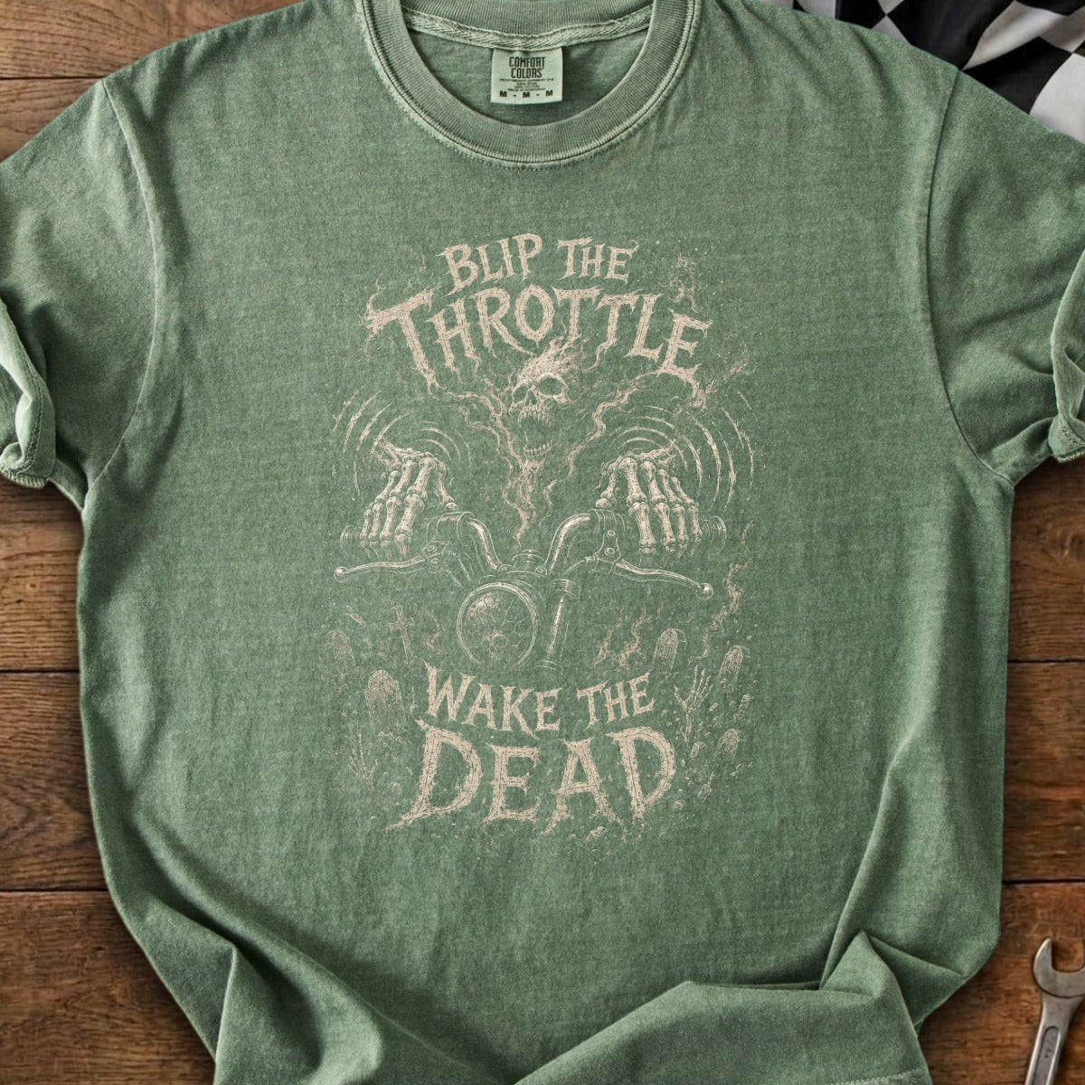 Green t-shirt with a skull and skeleton hands on a motorcycle graphic. Text reads "Blip the Throttle Wake the Dead".