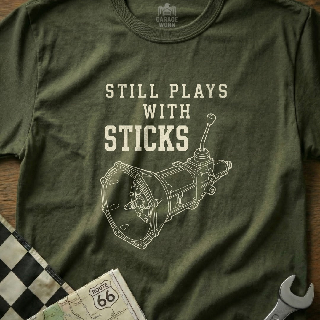 T-shirt with illustration of a manual transmission and text "Still Plays with Sticks".