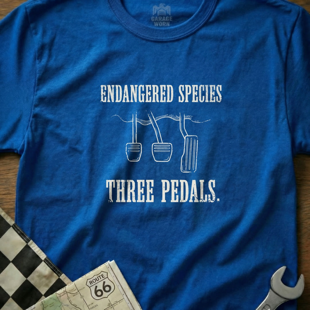 Blue t-shirt with "ENDANGERED SPECIES THREE PEDALS" text and car pedals graphic.