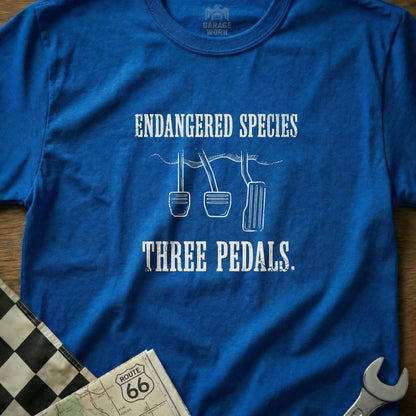 Blue t-shirt with "ENDANGERED SPECIES THREE PEDALS" text and car pedals graphic.