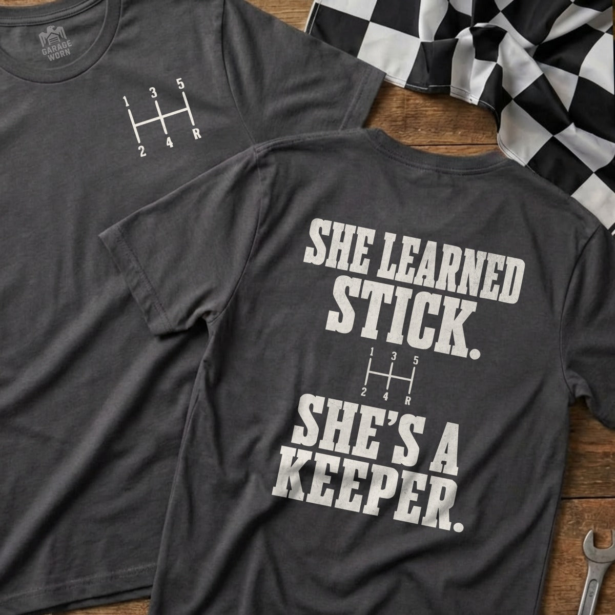Dark grey t-shirt with a 5-speed manual shift pattern and "She learned stick. She's a keeper."