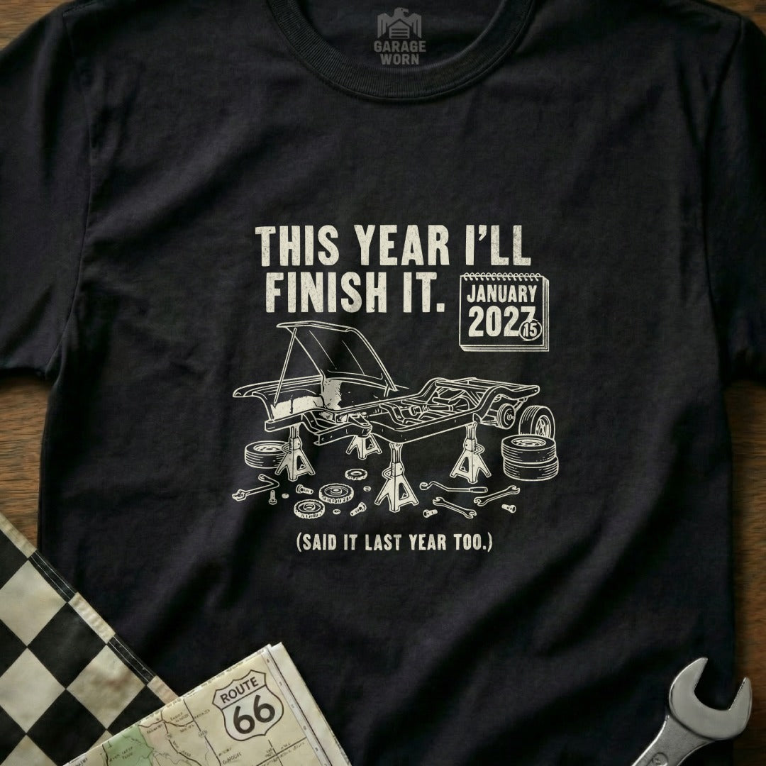 T-shirt with "This year I'll finish it. January 2027" and car under repair graphic.