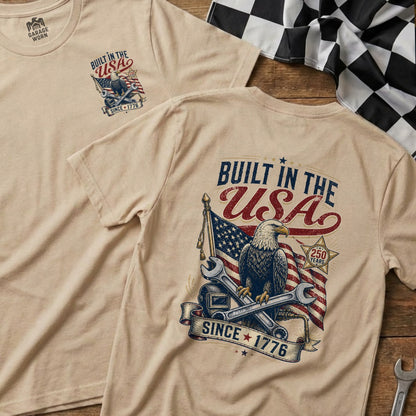 Tan t-shirt with "Built in the USA Since 1776" graphic featuring an eagle, flag, and tools.
