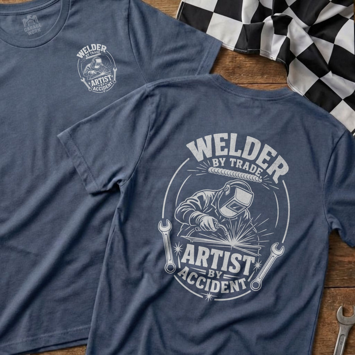 Blue t-shirt with a graphic of a welder and the text "Welder by Trade, Artist by Accident".