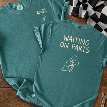 Teal t-shirt with "WAITING ON PARTS" text and a stick figure holding a bolt.