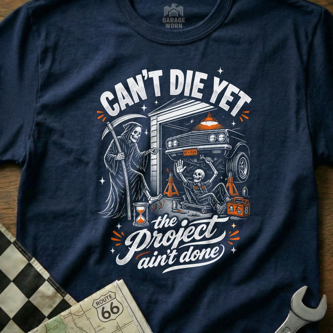 Grim Reaper points at skeleton working on car, "Can't Die Yet, The Project Ain't Done."