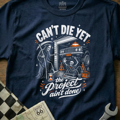 Grim Reaper points at skeleton working on car, "Can't Die Yet, The Project Ain't Done."