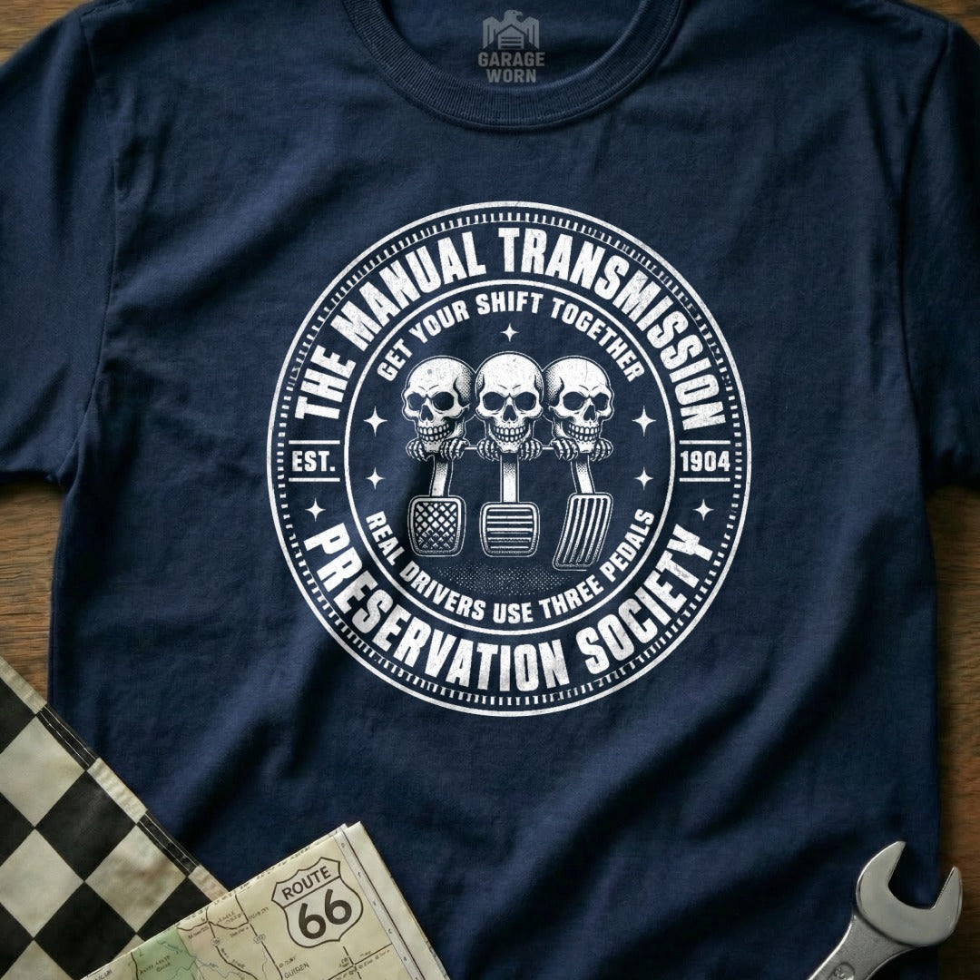 Navy t-shirt with "Manual Transmission Preservation Society" circular graphic and three skulls.