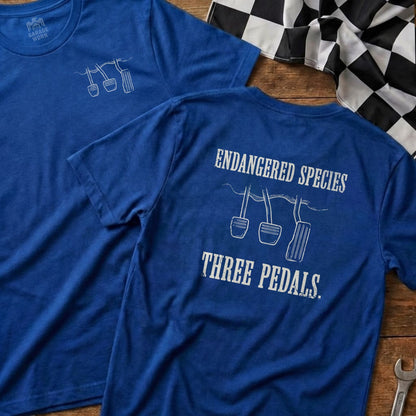 Blue t-shirt with "Endangered Species Three Pedals" and car pedals graphic.