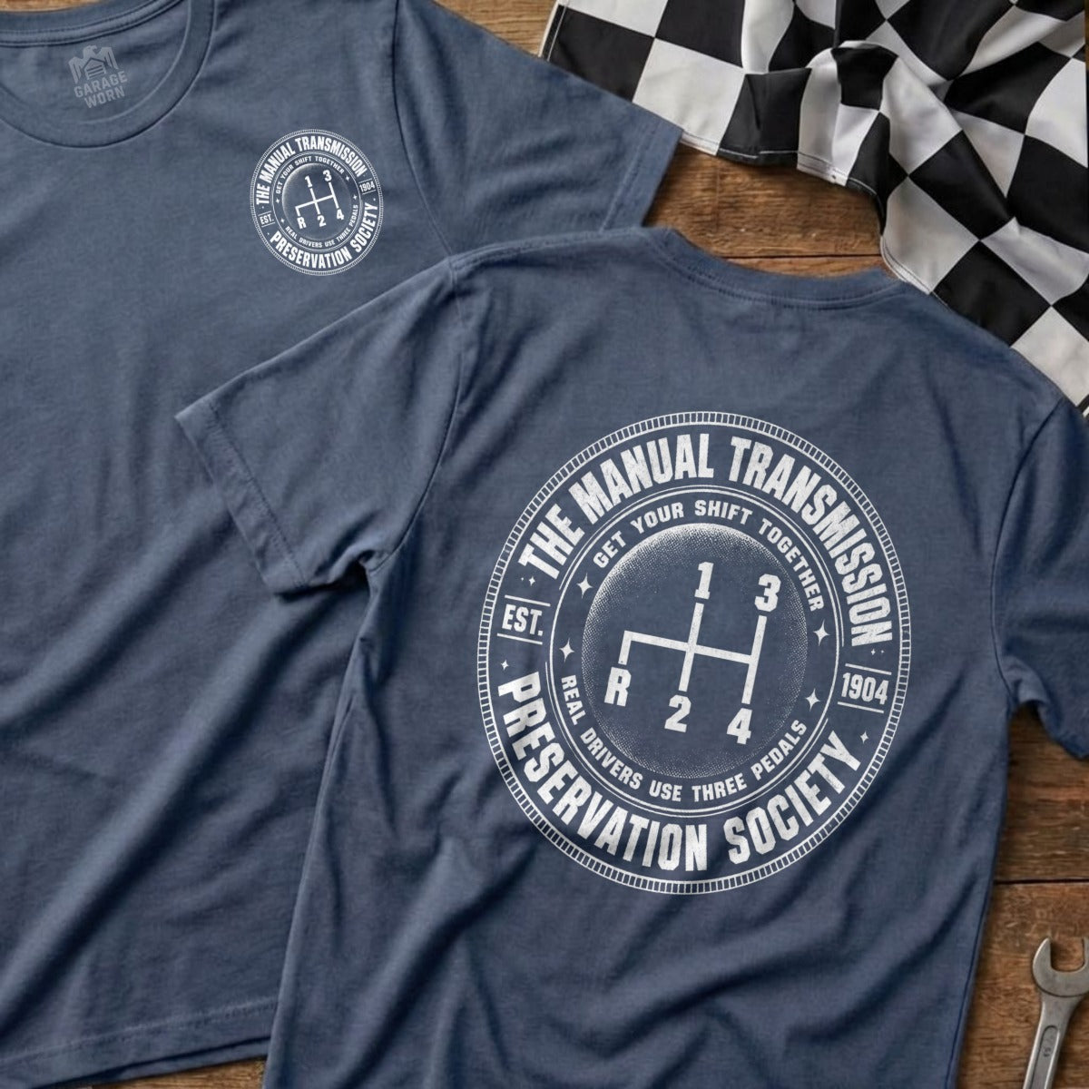 Blue t-shirt with a circular graphic of a manual transmission shift pattern and text.
