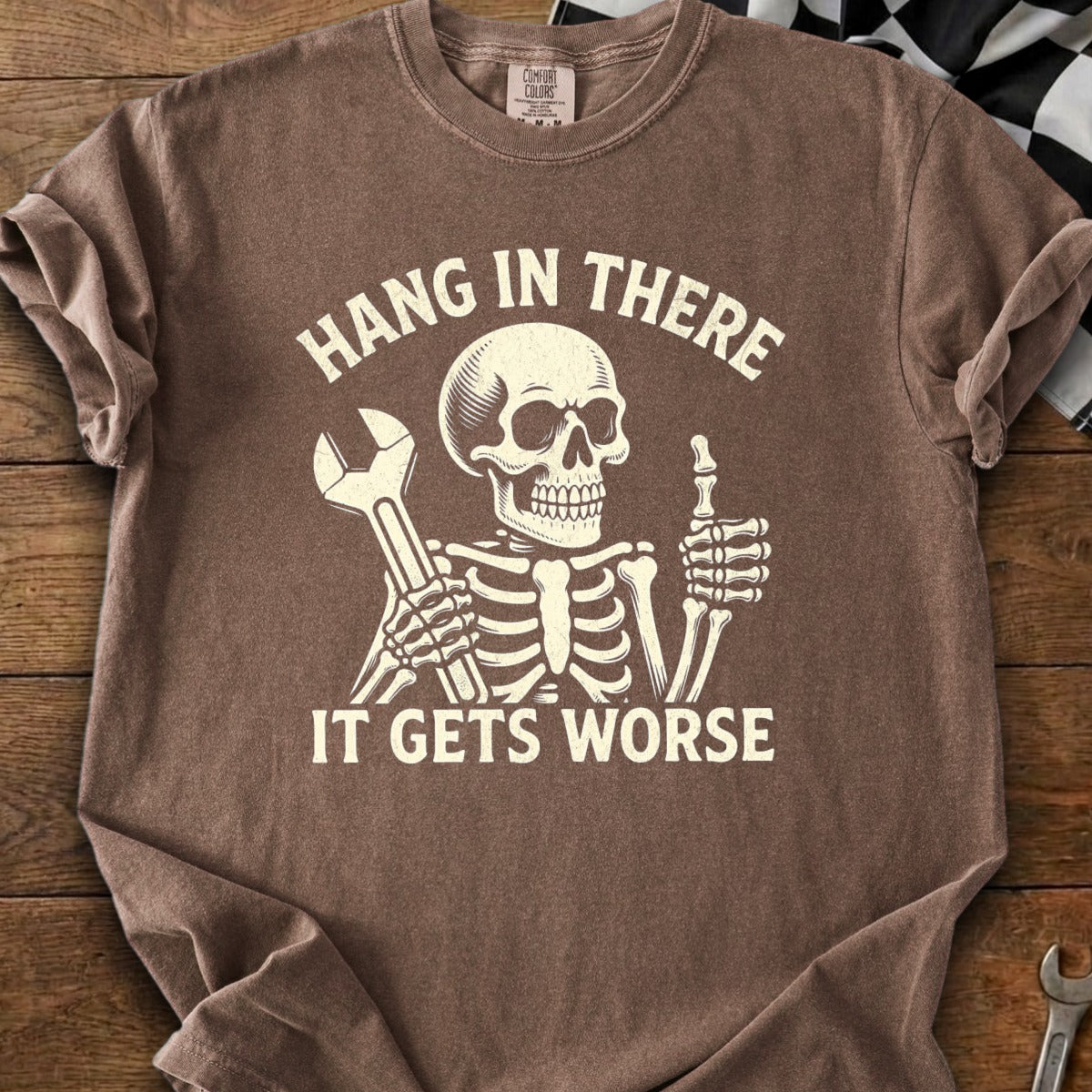 Brown t-shirt graphic of skeleton holding wrench and giving thumbs up with text.