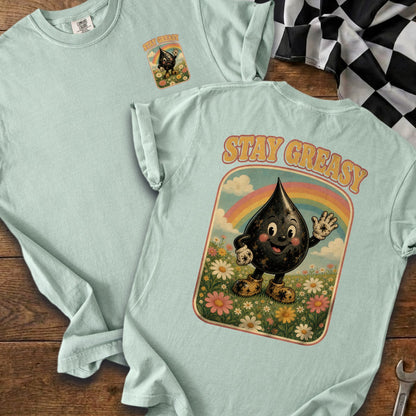 Light blue t-shirt with "Stay Greasy" graphic of a smiling oil drop in a field under a rainbow.