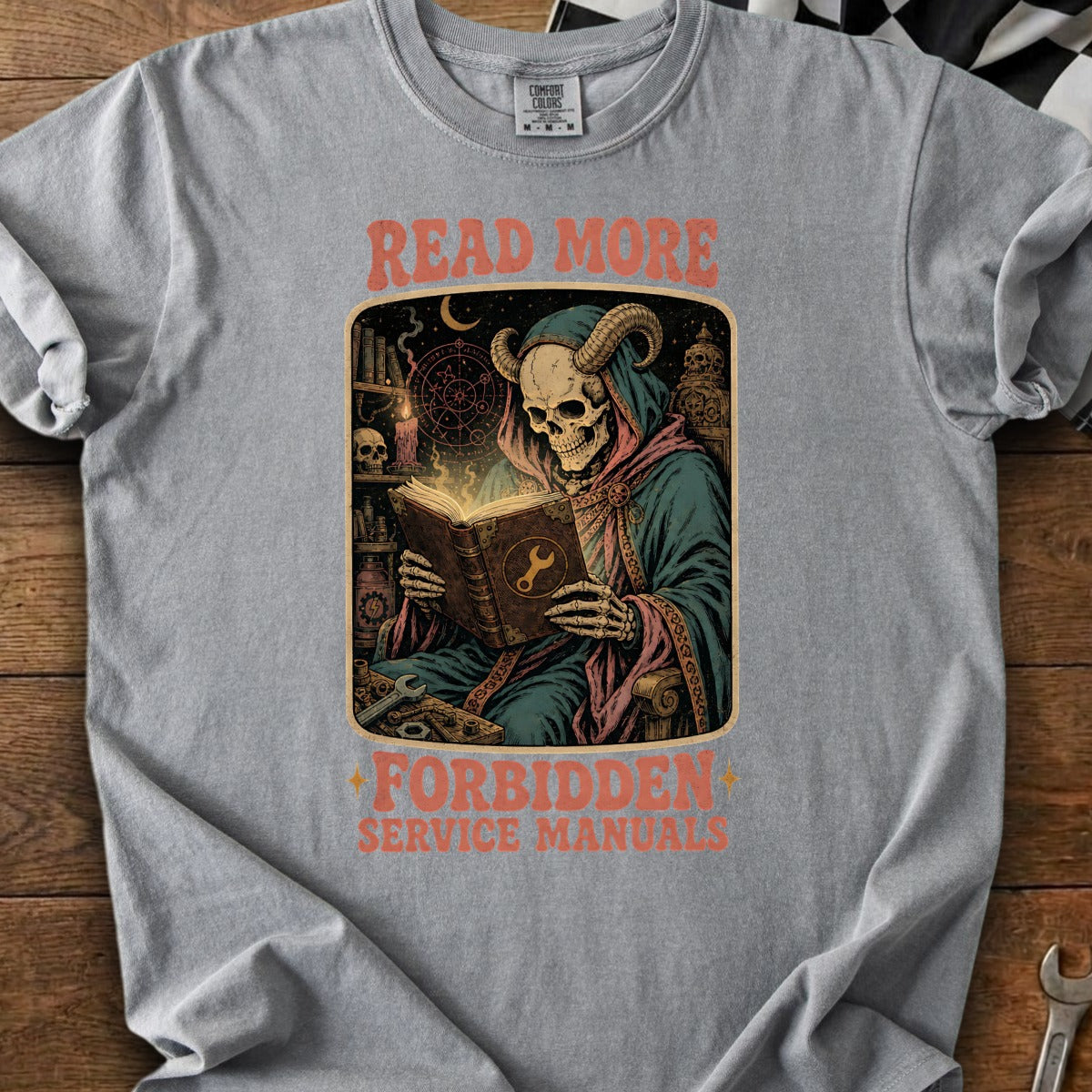 Graphic tee with skull and horns reading a book; "Read More Forbidden Service Manuals" text.