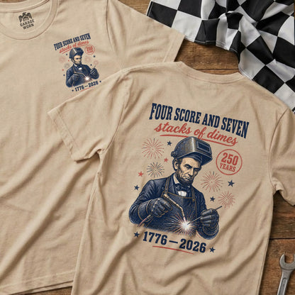 T-shirt featuring Abraham Lincoln welding, with text "Four Score and Seven stacks of dimes 1776-2026".
