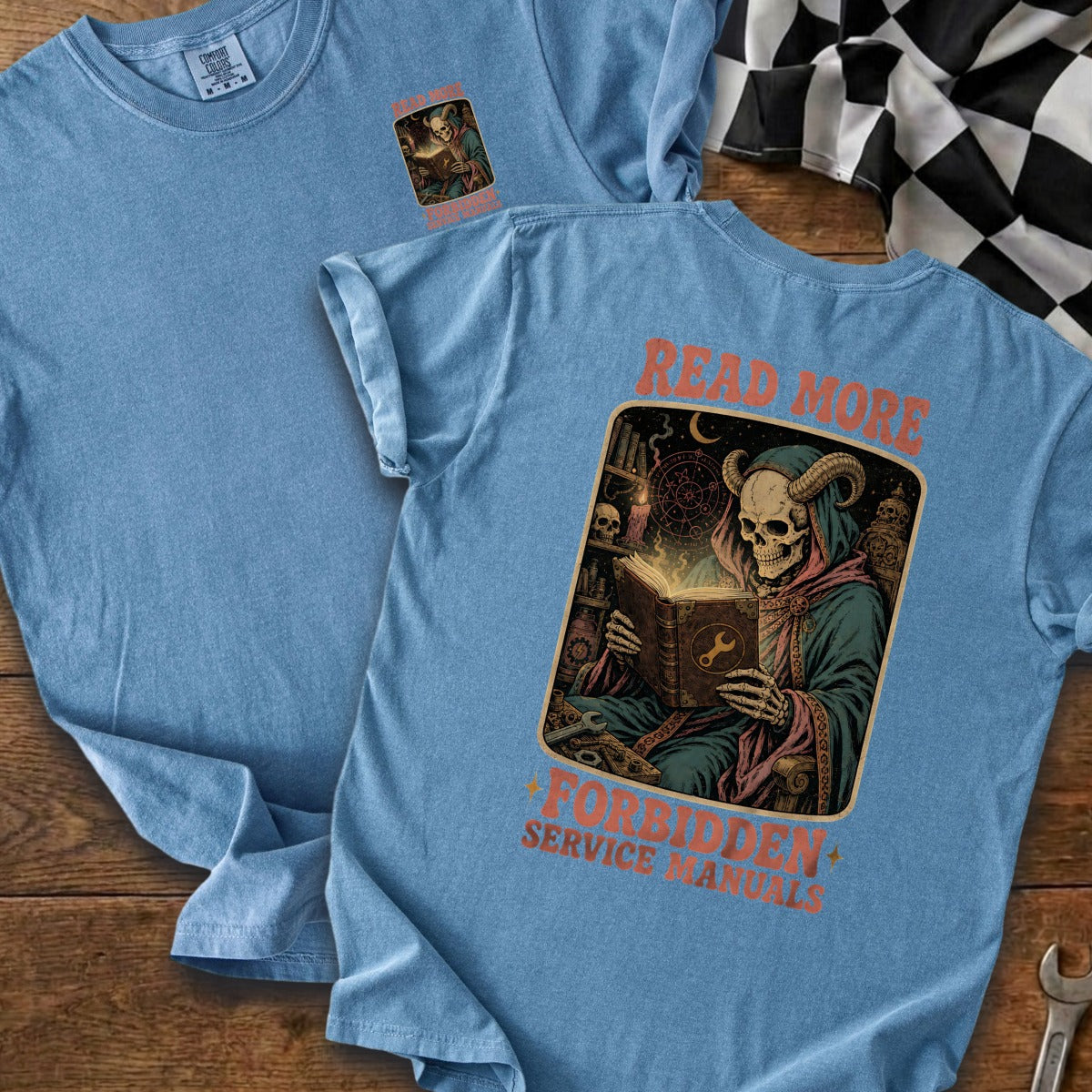 Blue t-shirt with skeleton in robes reading book, text "READ MORE FORBIDDEN SERVICE MANUALS".