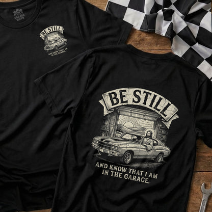 Black t-shirt with "Be Still and Know That I Am In The Garage" text and car graphic.