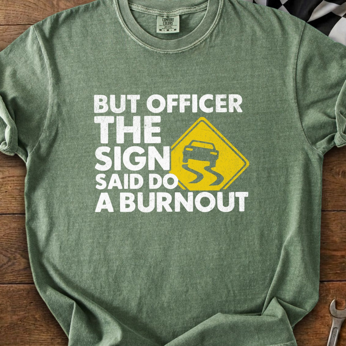Green t-shirt with text "BUT OFFICER THE SIGN SAID DO A BURNOUT" and a slippery road sign.