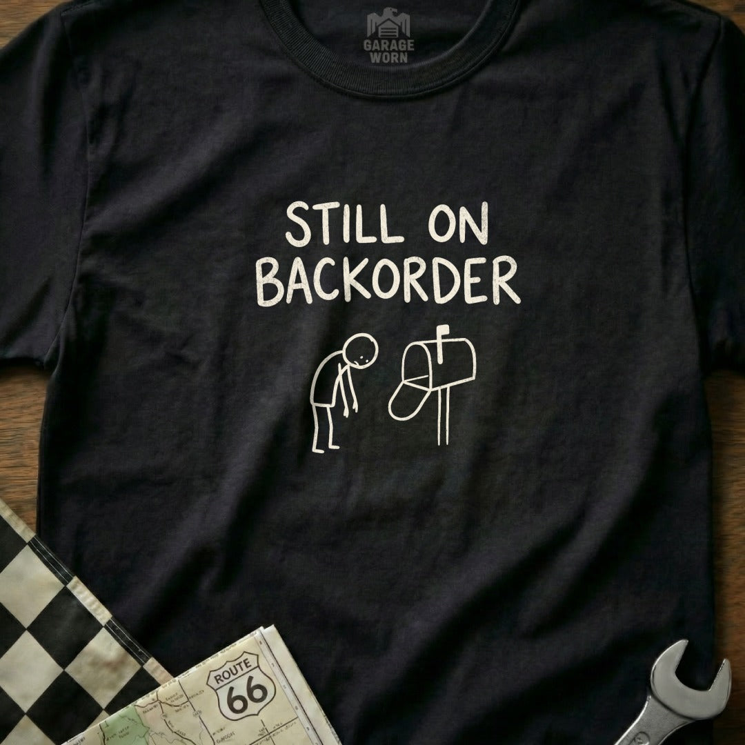 Black t-shirt with "Still on Backorder" text and stick-figure illustration.