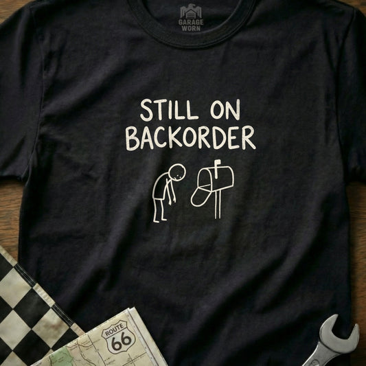 Black t-shirt with "Still on Backorder" text and stick-figure illustration.
