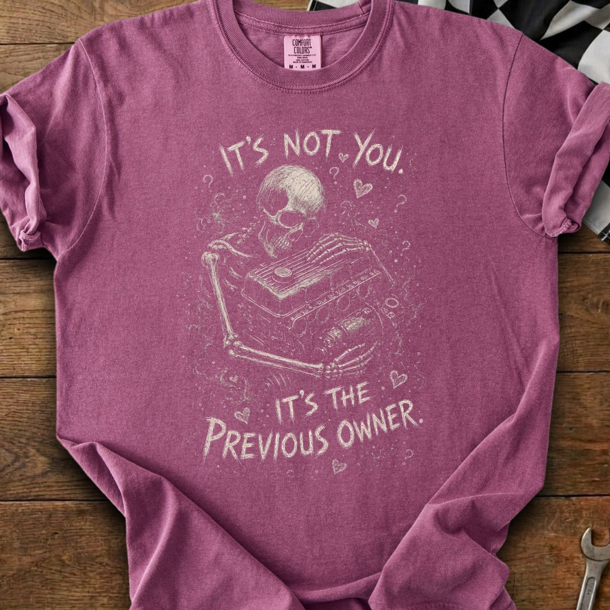 Skeleton holding engine on maroon t-shirt with text "It's not you. It's the previous owner."