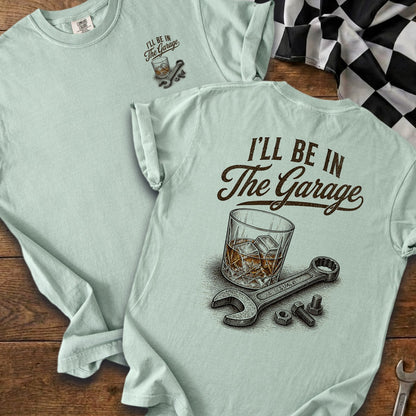 Light blue t-shirt with "I'll be in The Garage" text and whiskey glass, wrench, bolts.
