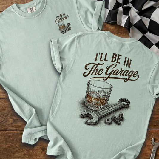 Light blue t-shirt with "I'll be in The Garage" text and whiskey glass, wrench, bolts.