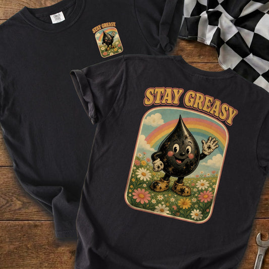 Black t-shirt with a graphic of a smiling oil drop character in a flower field under a rainbow and the text "STAY GREASY".