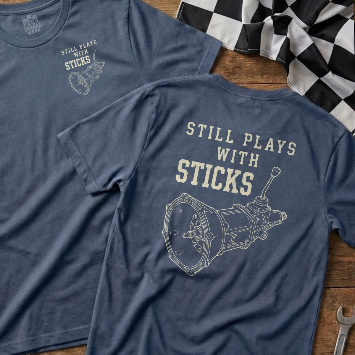 Blue t-shirt with "Still Plays with Sticks" and a manual transmission graphic.