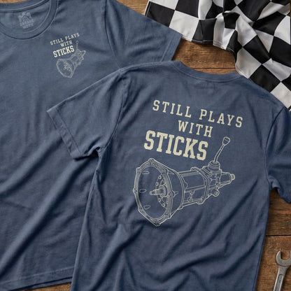 Blue t-shirt with "Still Plays with Sticks" and a manual transmission graphic.