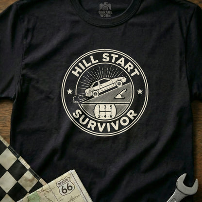 Black t-shirt with "Hill Start Survivor" circular graphic and a car on an incline.