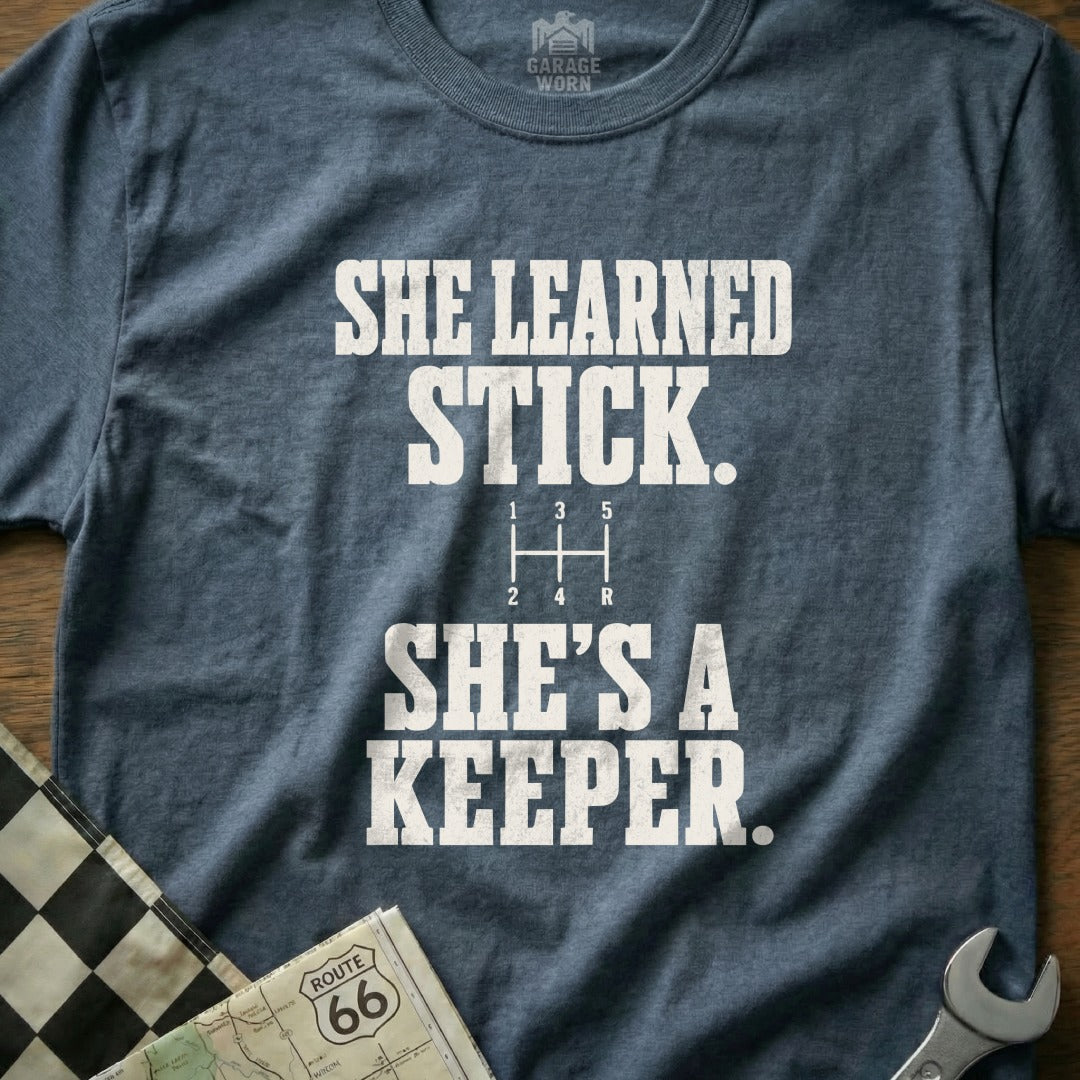 T-shirt with "She Learned Stick. She's A Keeper." and a gear shift pattern.