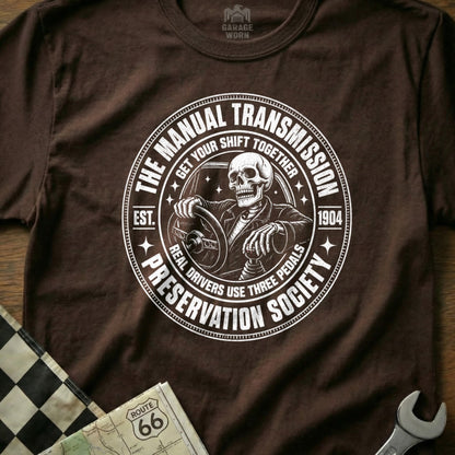 Brown t-shirt with "The Manual Transmission Preservation Society" circular graphic and a skeleton driving.