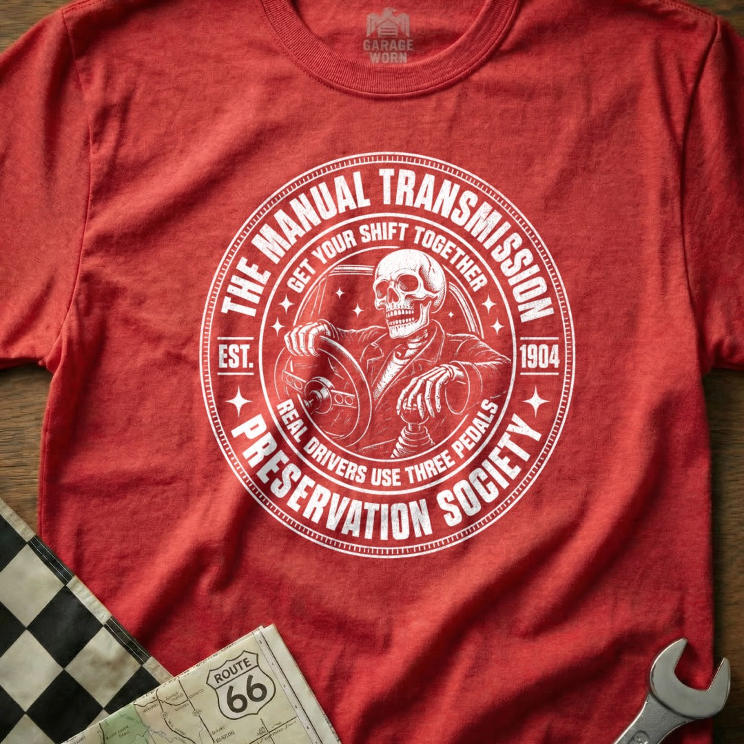 Red t-shirt with a circular graphic featuring a skeleton driving and text: "The Manual Transmission Preservation Society".