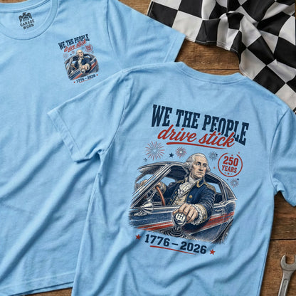 Light blue t-shirts with Washington driving, "WE THE PEOPLE drive stick," and "1776-2026."