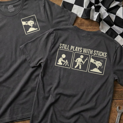 Dark t-shirt with "STILL PLAYS WITH STICKS" and three icons.