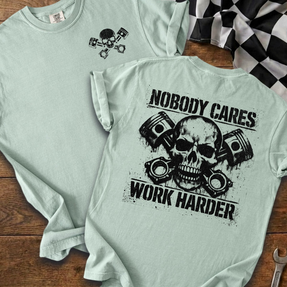 Light blue t-shirt with skull and pistons graphic, text "NOBODY CARES WORK HARDER".
