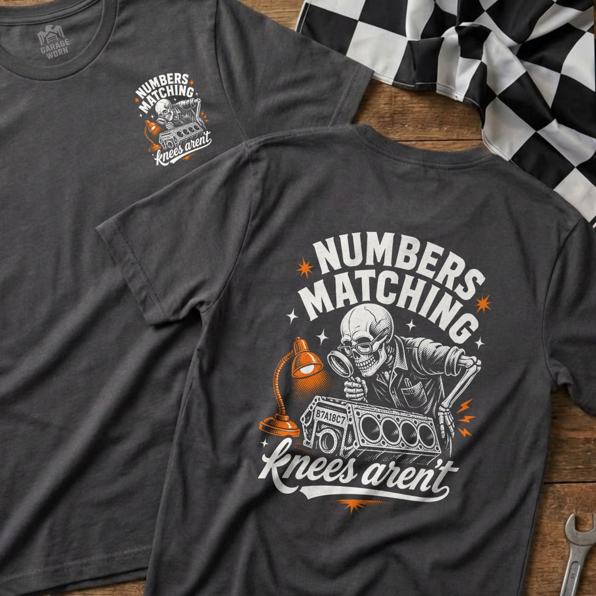 Dark gray t-shirt with a graphic of a skeleton examining an engine with a magnifying glass, text reads "Numbers Matching, Knees Aren't".