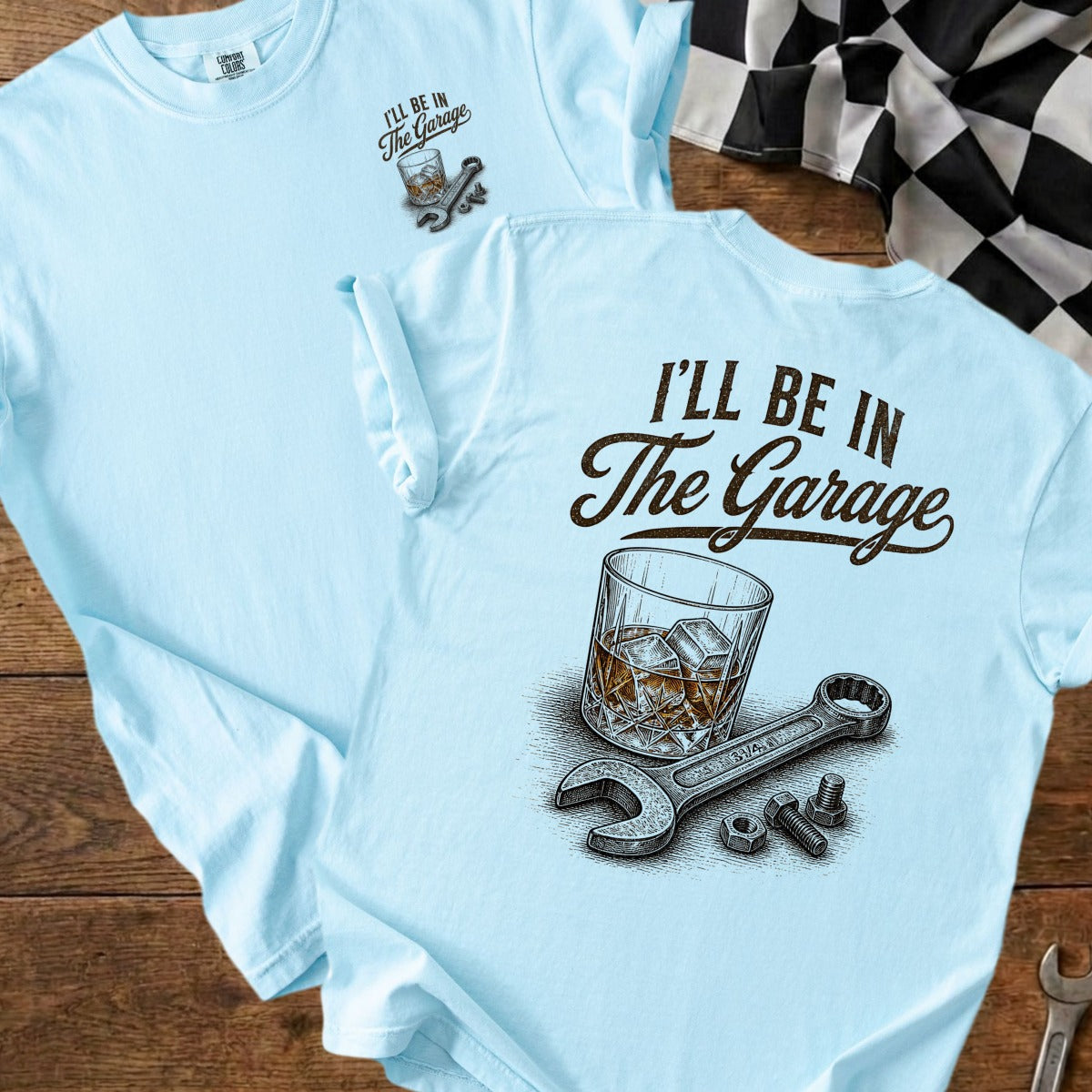Light blue t-shirt with "I'll Be In The Garage" text, whiskey glass, wrench, nuts, and bolts.