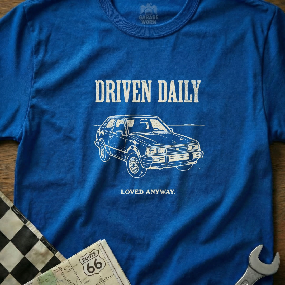 Blue t-shirt with white graphic of a car and text "DRIVEN DAILY LOVED ANYWAY."