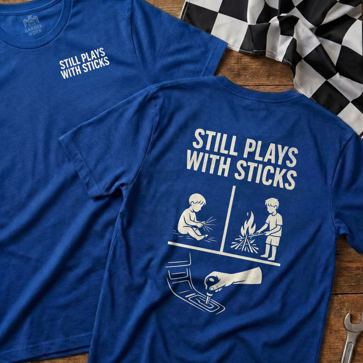 Blue t-shirt with "Still Plays With Sticks" and illustrated scenes.