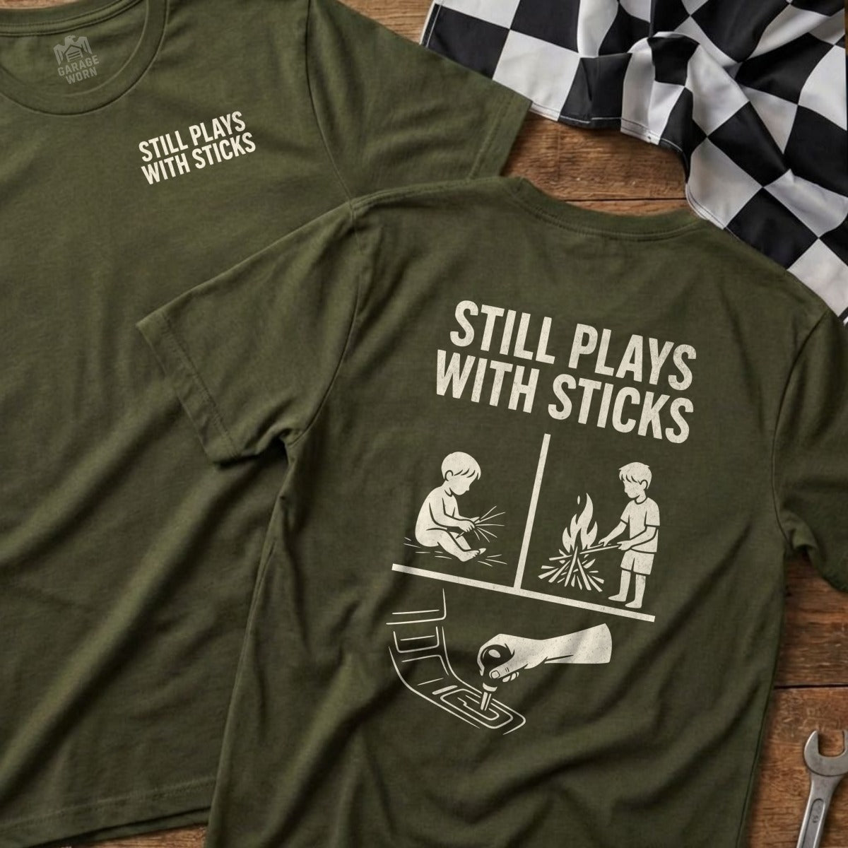 Olive green t-shirt with "STILL PLAYS WITH STICKS" and contrasting graphic.