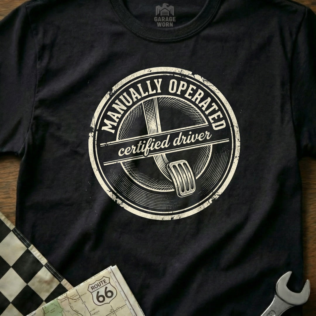 Black t-shirt with "Manually Operated Certified Driver" text and clutch pedal graphic.
