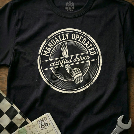 Black t-shirt with "Manually Operated Certified Driver" text and clutch pedal graphic.